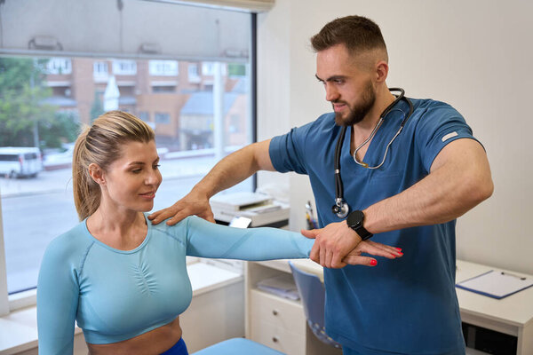 Male traumatologist checking muscle strength and coordination of female client, making test checking her posture, rehabilitation centre
