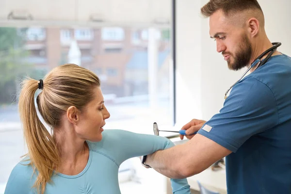 Close-up bearded neurology specialist checking female patient reflexes, knocking with hammer on her elbows, medical test to check muscles and body condition