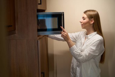 Uzun saçlı ve güzel manikürlü güzel bir kadın. Kapalı alanda dururken mikrodalga kullanıyor.