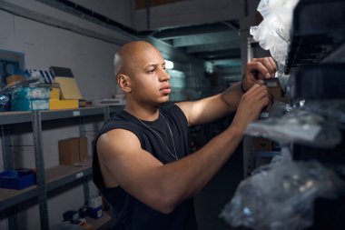 Araba tamircisi, depo, motorlu taşıt servis istasyonundaki arabaların onarımı ve bakımı için gerekli yedek parça ve ayrıntıları kontrol ediyor.