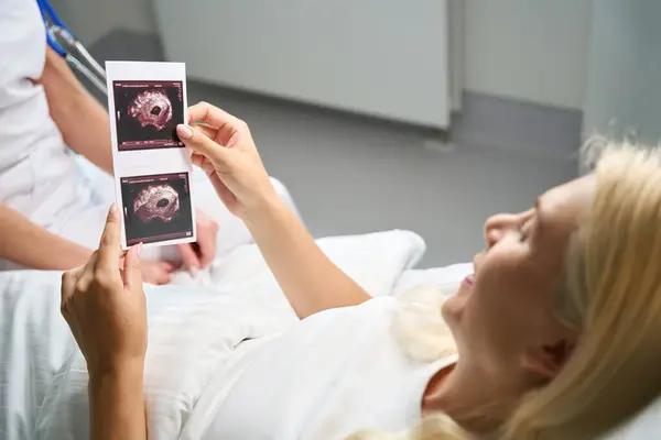 幸せな女性患者は彼女の手で超音波写真を保持し 彼女は病院の部屋で医者と通信する — ストック写真