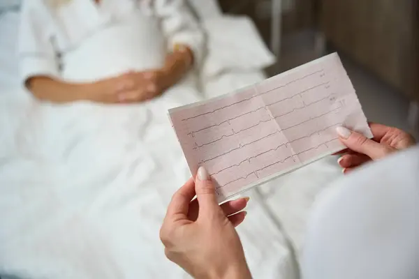 電気カルダイオグラムを有する病院の部屋の医師は 女性患者が病院のベッドに横たわっています — ストック写真