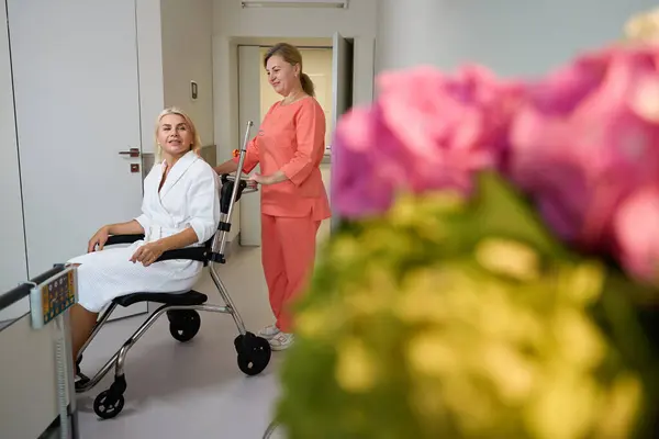 卫生工作者把一名坐在轮椅上的病人和一名穿着医院长袍的妇女带到医院病房 — 图库照片