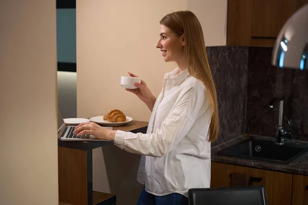 Mujer Feliz Sosteniendo Taza Café Mientras Usa Ordenador Portátil Pie — Foto de Stock