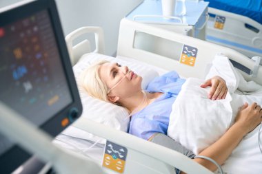Ameliyattan sonra kadın, hastaların hayati fonksiyonlarını izlemek için modern ekipmanlarla dolu bir odada yatıyor.