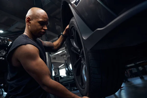 African American auto-mechanic changing seasonal tires and doing tire balancing, checking suspension condition, motor vehicle service station