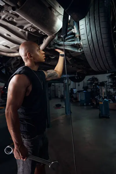 African American repairman concerned about play and creaking in bottom, auto-mechanic checking condition of suspension and hubs, quality of wheel fastenings