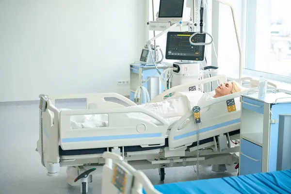 숙녀는 환자의 중요한 기능을 모니터링하기위한 기기와 병동에서 특별한 침대에 — 스톡 사진