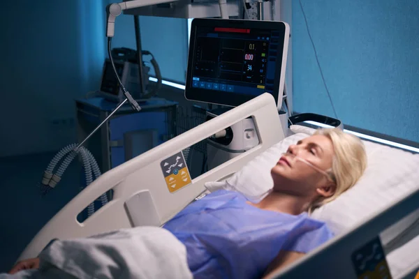 ブロンドの女性は集中治療ユニットの術後ベッドに横たわり 彼女は酸素機械に接続されています — ストック写真