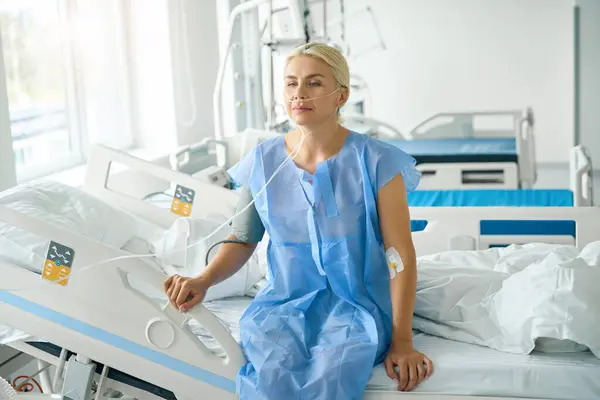 身着医院服装的女士坐在康复室的床上 与支持和监控装置相连 — 图库照片