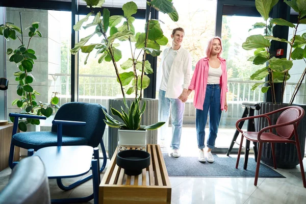 stock image Guy and his girlfriend, holding hands, enter design studio, there is lot of furniture and living plants in the room