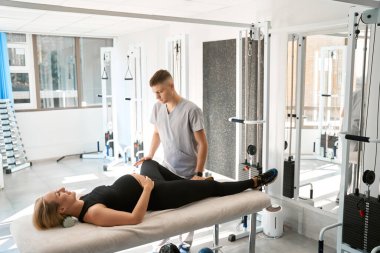 Rahat bir kayropraktik seansında gülümseyen anne, ayakları üzerinde çalışan bir kayropraktör.