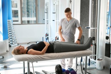 Fizyoterapist etkili bir basınç terapisi uyguluyor. Bir kadın özel bir süpürge pantolon giyiyor.