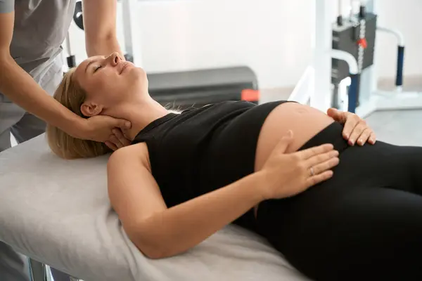 Massage therapist conducts a manual therapy session for a pregnant woman, a woman lies on a massage table