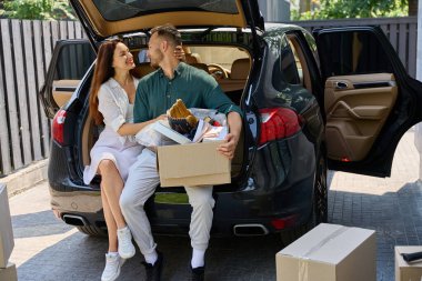 Mutlu eşler bir arabanın bagajında oturuyorlar, yeni bir kır evine taşınıyorlar.