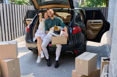 Elinde anahtar olan bir kadın ve kocası bir arabanın bagajında dinleniyor.