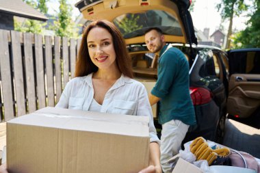 Gülümseyen kadın bagajdan bir kutu eşya taşır, o ve kocası arabayı boşaltır.