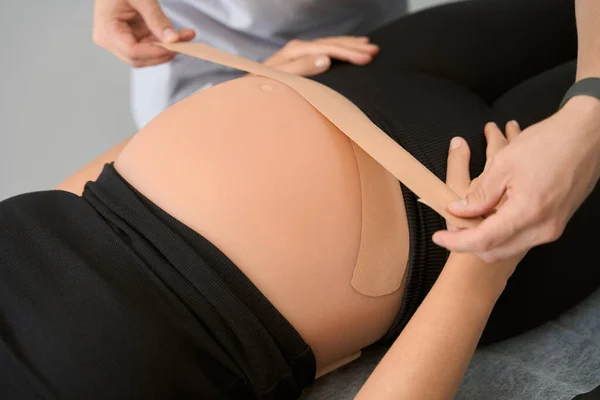 Specialist kinesiotherapist taps the belly of a pregnant woman, the client lies on the massage table
