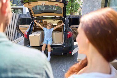 Neşeli çocuk ailesiyle bir kır evine taşınıyor, kutularda eşyalar var.