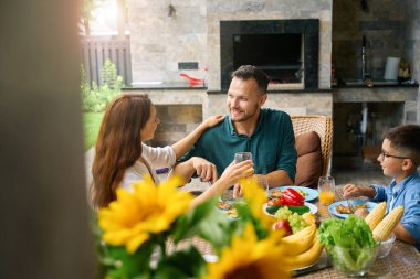 Mutlu aile, baba, anne ve oğul, terasta öğle yemeği, masada lezzetli sağlıklı yemekler.