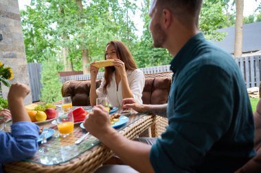 Güzel bir kadın iştahla mısır yer, aile bir kır evinin terasında öğle yemeği yer.