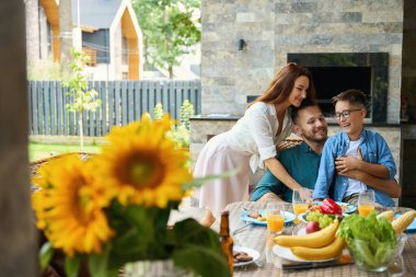 Dost canlısı aile yemek masasında iletişim kurar. Masada çok güzel ayçiçekleri vardır.