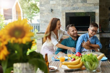 İnsanlar yemek masasında neşeyle gülüyor, masada güzel ayçiçekleri var.