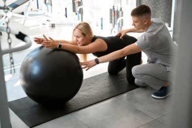 Sevimli hamile kadın bir eğitmenin gözetiminde egzersiz yapıyor, rahat spor kıyafetleri giyiyor.