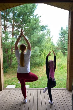 Arka plan anne ve kızı ağaç duruşu ya da Vrikshasana, açık havada yoga, temiz havanın ve güzel doğanın tadını çıkarma, dengelemeyi öğrenme