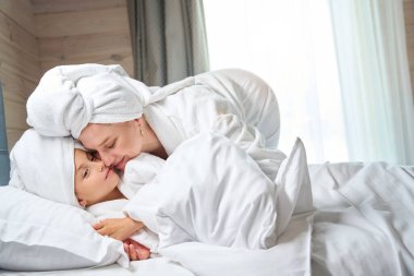 Kafasında havluyla oldukça temiz bir anne yumuşak bornozlu tatlı kızını öpüyor kızlar hafta sonunu kaplıcada birlikte geçiriyorlar.