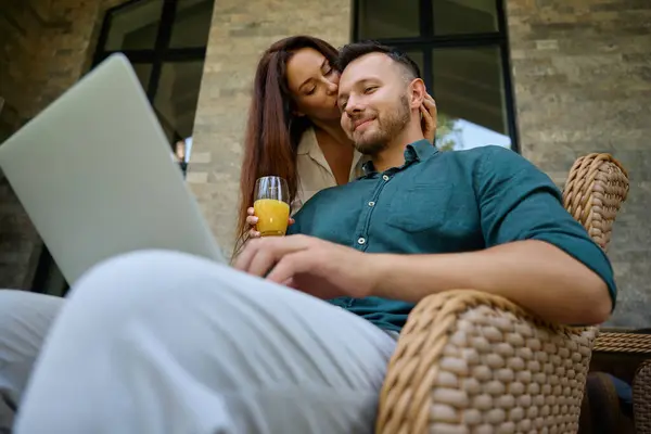 Muž Sedí Proutěném Křesle Pracuje Laptopu Jeho Žena Něžně Objímá — Stock fotografie