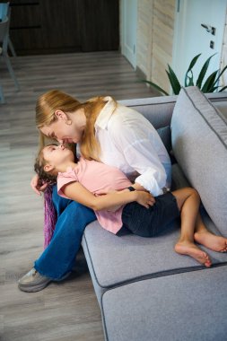 Anne-kız kucaklaşıp sarılıyor, oturma odasında kanepede oturup eğleniyor, birlikte zaman geçiriyorlar, anne-kız arasındaki ilişki...