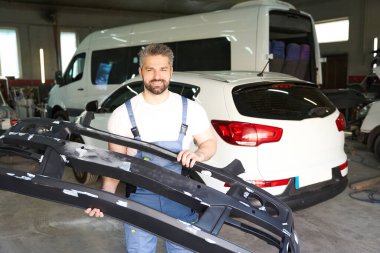 Gülümseyen araba tamircisi. Ön tampon kapaklı. Garajda duruyor.