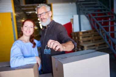 İnsanlar bir depoda kutuların yanında duruyor, bir adamın elinde kilit var.