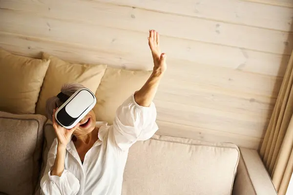 ハッピー年金は仮想ゲームをプレイする部屋のソファに座って 彼女は仮想現実のメガネを使用しています — ストック写真
