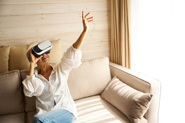 Happy lady in the room on the sofa playing a virtual game, she uses virtual reality glasses