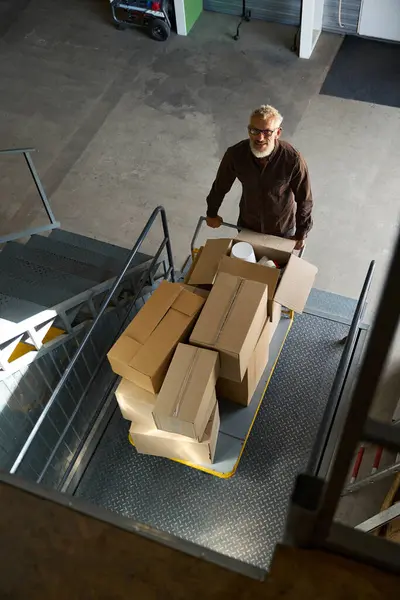 Man lifts a cart with things on a freight elevator, there are a lot of cardboard boxes on the cart