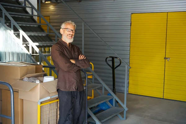 Bearded man stands by a cargo cart, there are boxes with things on the cart