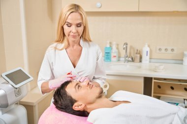 Müşteri kozmetoloji kliniğinde güzellik iğnesi yaptırıyor, doktor ince bir iğne kullanıyor.