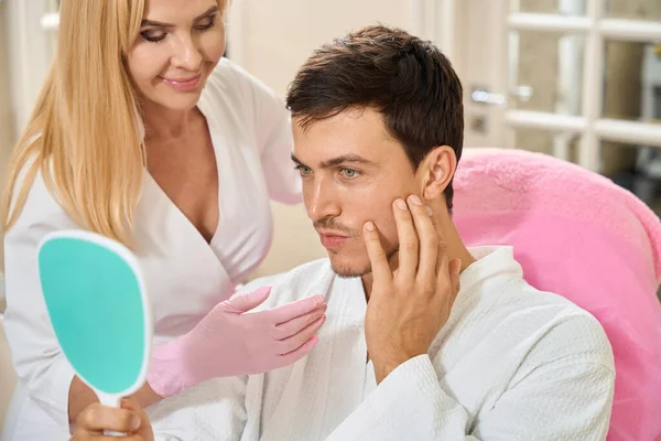 Tevreden Man Bij Een Cosmetologen Afspraak Onderzoekt Zijn Gezicht Spiegel — Stockfoto