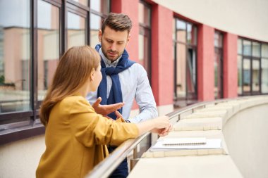 Yöneticiler büyük bir ofis binasının balkonunda iletişim kuruyor, rahat kıyafetler giyen insanlar.