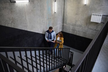 Meslektaşlar iş belgelerini inceliyor. Girişteki merdivenlerde, bir kadının dizüstü bilgisayarı var.