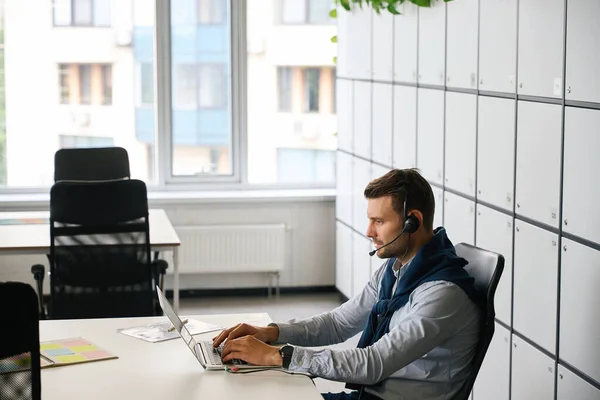 Freelancer with a laptop is located in the office area of a coworking space, he uses a headset