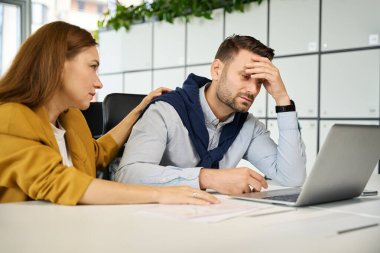 Genç müdür, üzgün bir iş arkadaşını teselli ediyor. İnsanlar büyük bir ofis masasında oturuyor.