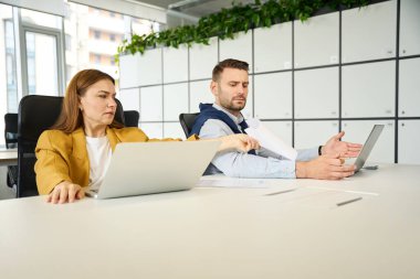 Tartışan meslektaşlar işyerlerinde otururken, insanlar büyük bir ofis masasında oturuyorlar.