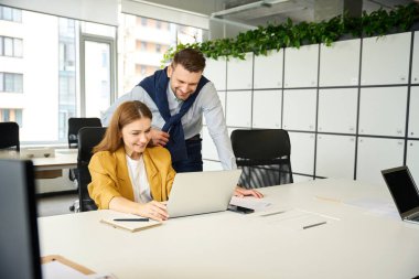 Yönetici genç bir çalışanın, bir kadının laptopta çalışmasını denetliyor.
