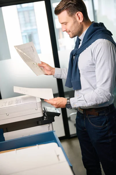 マネージャーは文書を使用するためにオフィス装置を使用します 彼は快適なカジュアルな服にあります — ストック写真