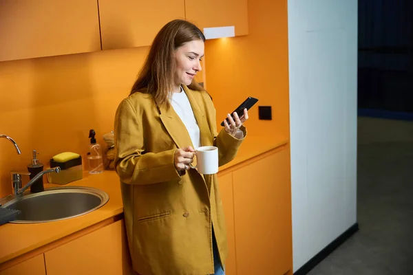 Employee with a cup of tea talks on the phone in the kitchen area of a coworking space