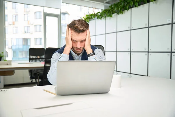 人は職場でノートパソコンの前に座り 頭痛に苦しんでいる — ストック写真