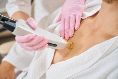 Bir güzellik salonunda, göğsünün lazerle alındığı bir erkek. Bir uzman koruyucu eldivenler üzerinde çalışıyor.